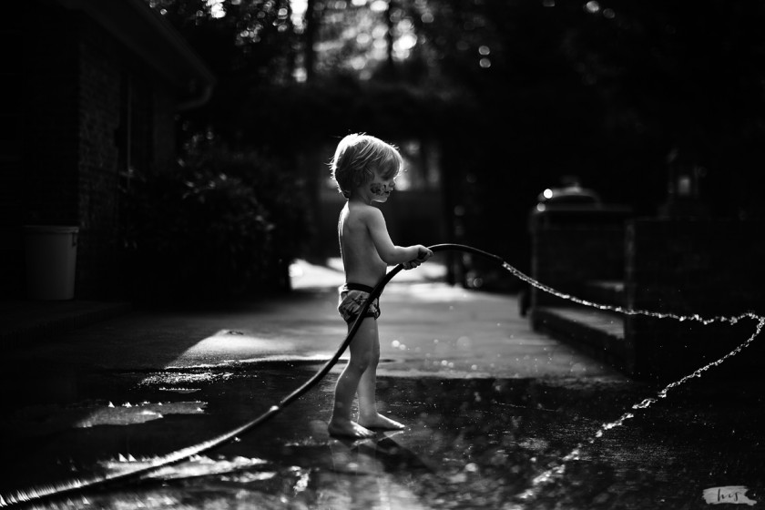 backlit photo of boy swing a water hose by Heather Stockett