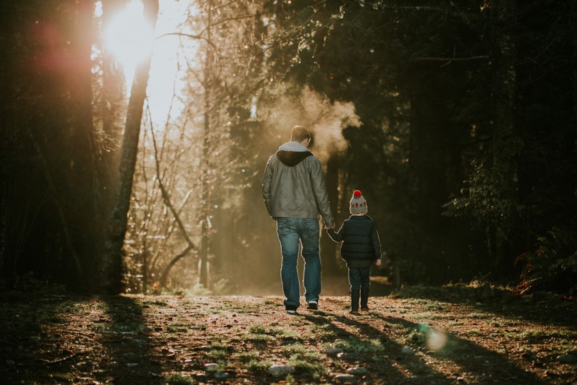 backlit photo of dad and son walking through the trees by Cassandra McCasley of Twist and Shutter Photography