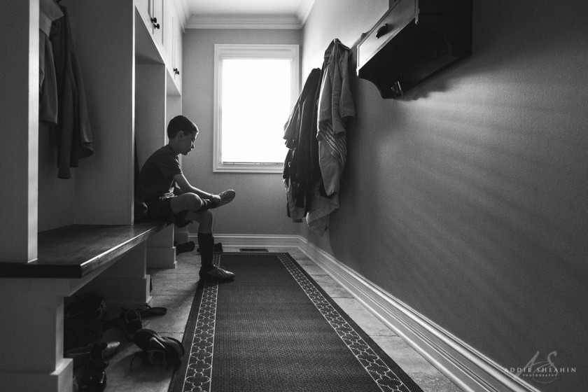 black and white photo of boy putting on his cleats by Addie Sheahin