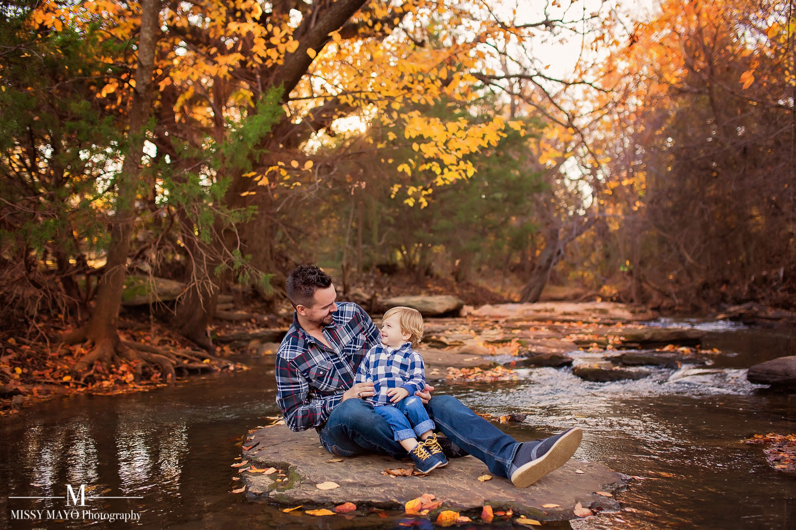 dad laughing with son at a creek during the fall by Missy Mayo
