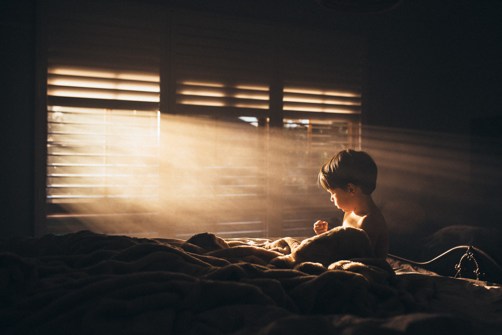 photo of boy sitting on bed with light shining in windows by Amy Shire